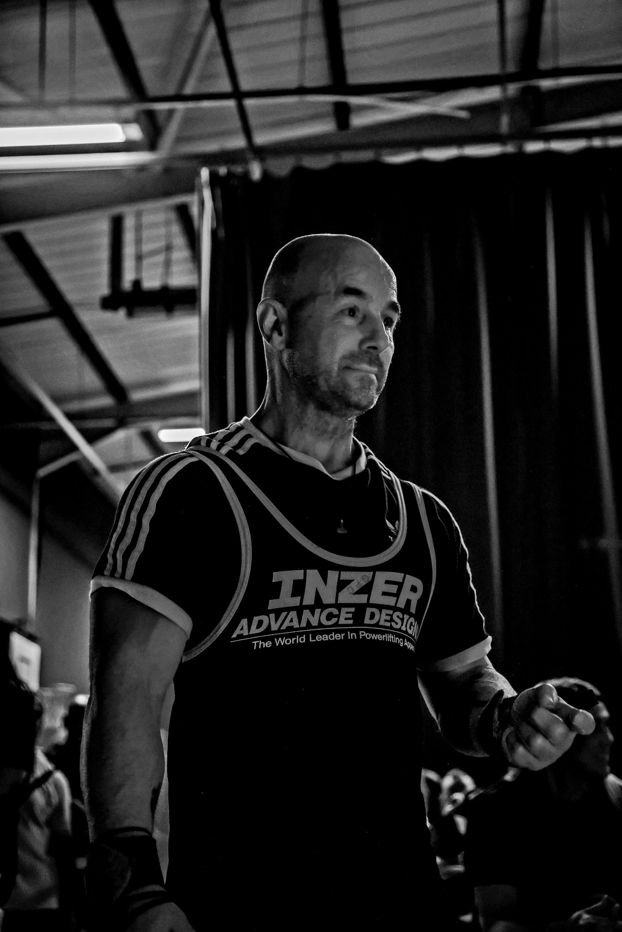Man wearing an 'INZER ADVANCE DESIGN' shirt in a gym setting