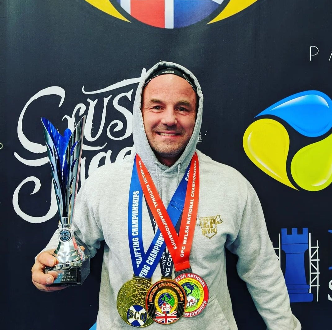 Graham dowers holding a trophy and medals in front of a branded backdrop